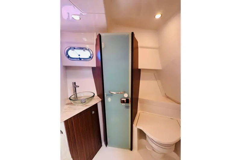 Slide: The Image of 2021 Pursuit OS 355 Offshore bathroom with glass sink, frosted door, and porthole window. - 35