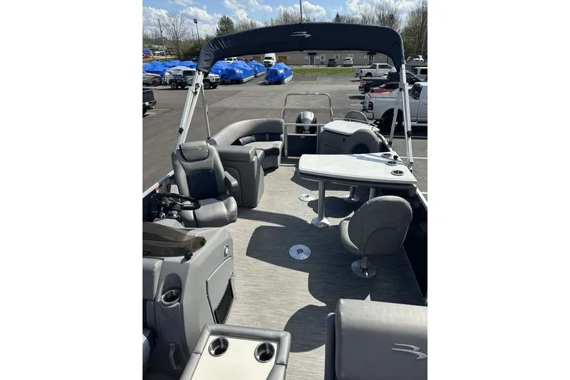 Slide: The Image of 2022 Bennington LPD pontoon boat interior with seating and table, parked outdoors. - 10