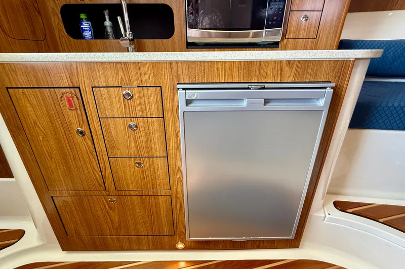 Slide: The Image of 2012 Pursuit OS 345 Offshore boat interior with wooden cabinetry, sink, and compact refrigerator. - 24