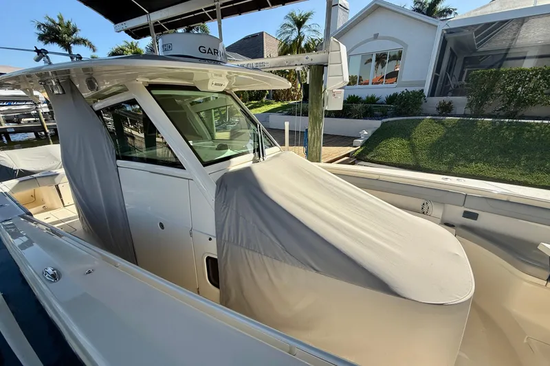 Slide: The Image of 2019 Scout 355 LXF boat docked, covered, with lush greenery and modern house in background. - 37