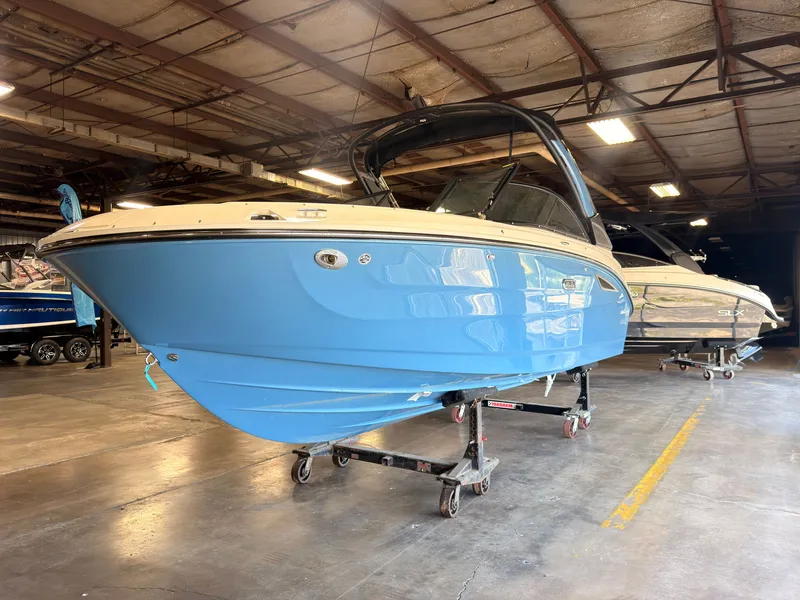 Slide: The Image of A blue and white 2026 Sea Ray SDX 230 Surf is on a dolly in a warehouse. - 2
