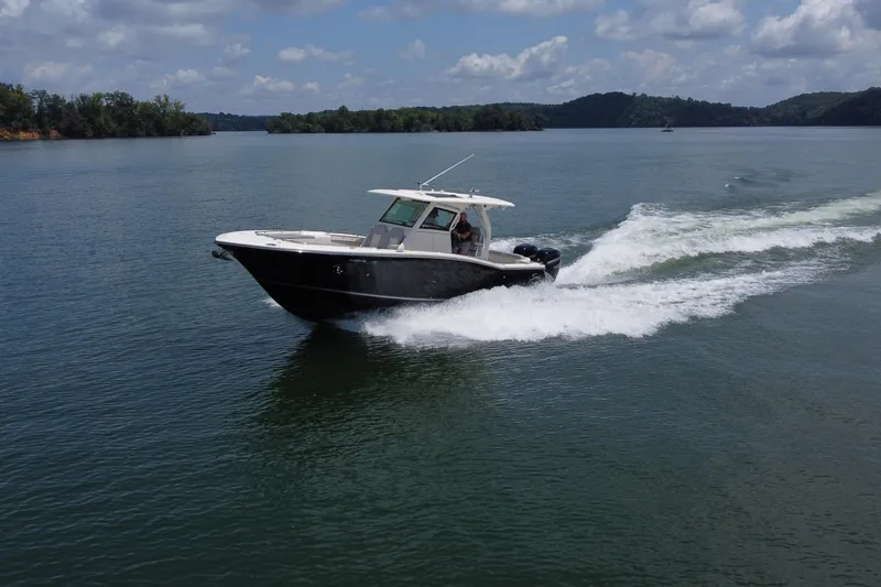 The Image of 2021 Scout 330 LXF boat cruising on calm water near lush greenery. - 1