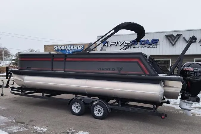 Slide: The Image of 2026 Viaggio x22u pontoon boat on trailer outside dealership in snowy setting. - 2