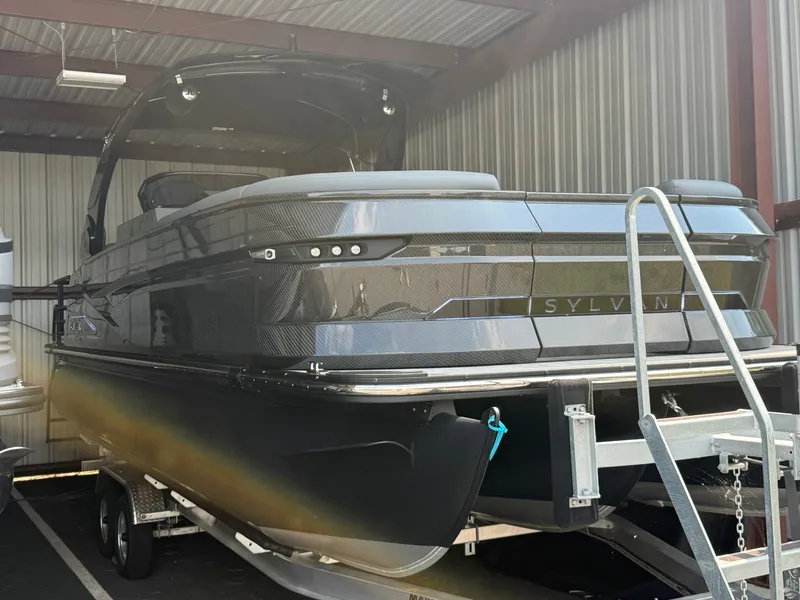 Slide: The Image of A 2027 Sylvan M-5 SLZ pontoon boat on a trailer in a covered area. - 0