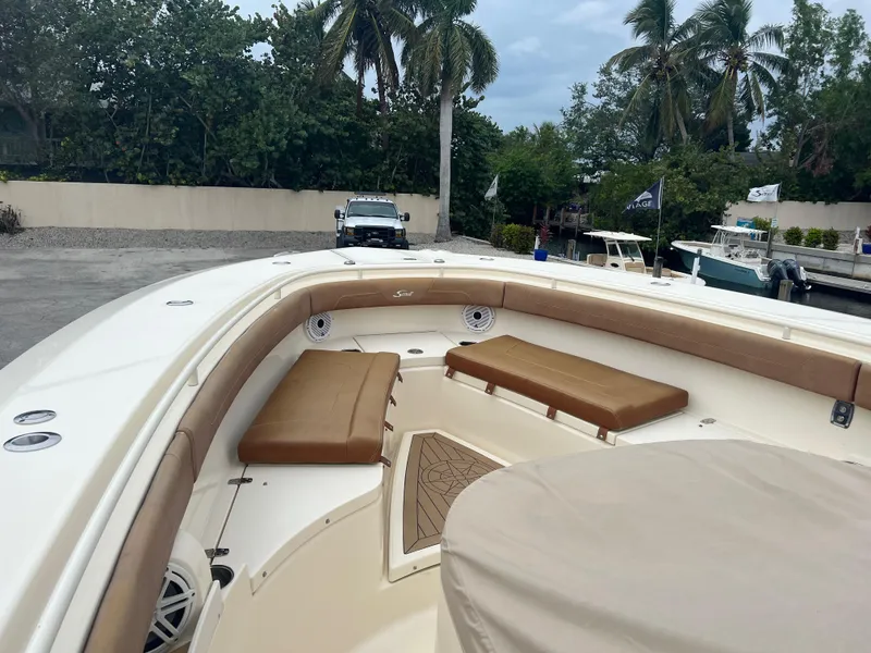 Slide: The Image of 2019 Scout 355 LXF boat with cushioned seating, docked near palm trees. - 18