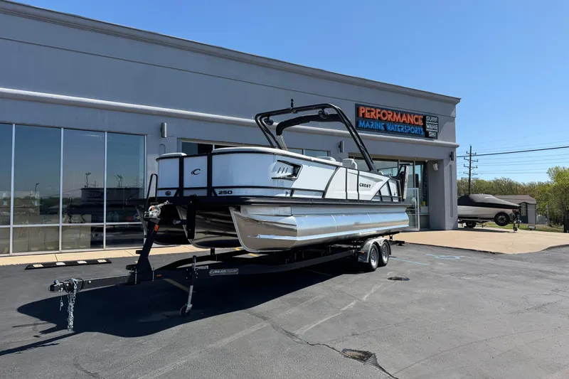 The Image of 2026 Crest Caribbean 250 SLS pontoon boat on trailer outside marine dealership. - 1