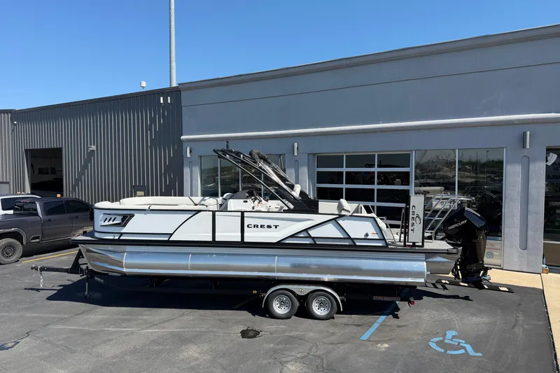 Slide: The Image of 2026 Crest Caribbean 250 SLS pontoon boat on trailer outside dealership. - 3
