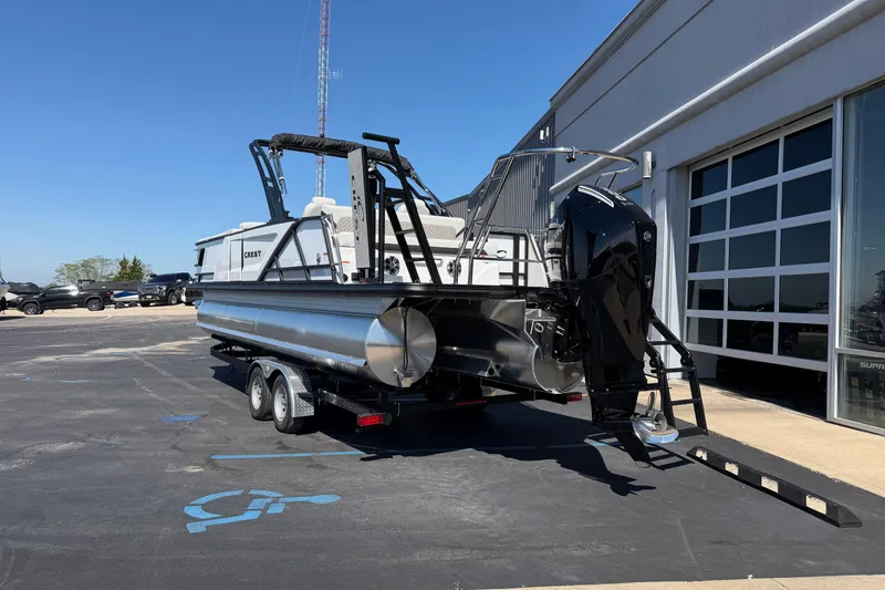 Slide: The Image of 2026 Crest Caribbean 250 SLS pontoon boat on trailer, parked outside dealership. - 4