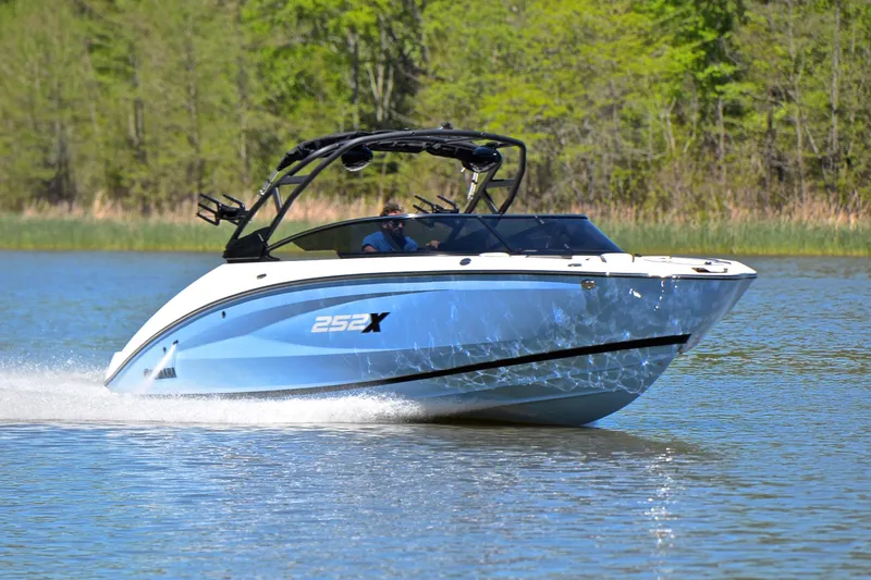 The Image of 2024 Yamaha Boats 252XE cruising on a serene lake with lush green trees in the background. - 1
