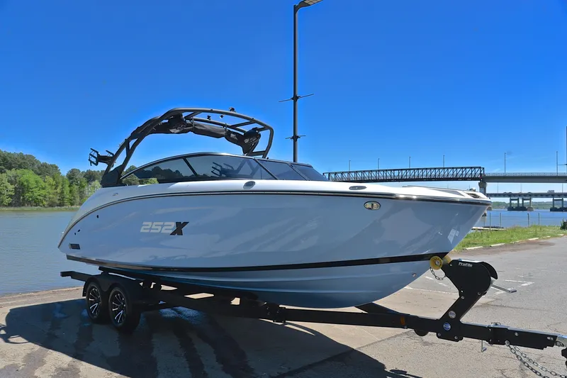 Slide: The Image of 2024 Yamaha Boats 252XE on trailer by a river under clear blue sky. - 16