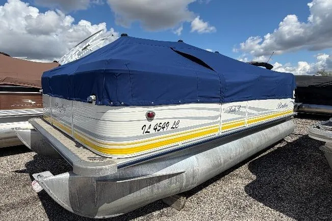 Slide: The Image of 2004 Bentley Pontoons 200 CRUISE with blue cover, parked on gravel under a cloudy sky. - 5