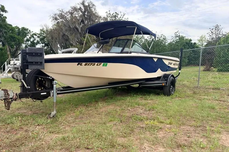 The Image of 2001 Nautique Sport Nautique 200 boat on trailer, parked on grass near a fence. - 0