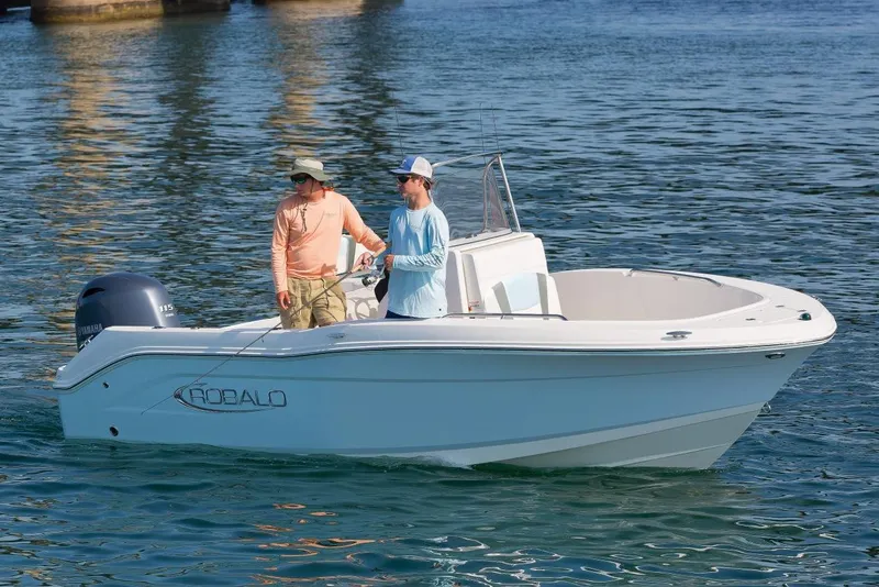 Slide: The Image of 2026 Robalo R180 Center Console boat with T-top, docked outdoors under blue sky. - 2