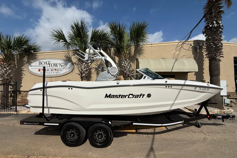 The Image of 2020 MasterCraft X22 boat on trailer, parked near palm trees and Boat Town sign. - 1
