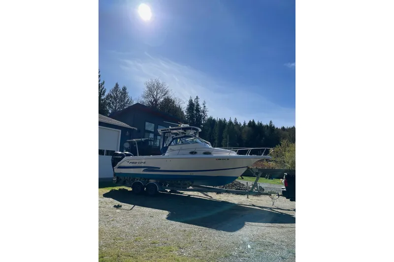 Slide: The Image of 2002 Pro-Line 260 Walkaround boat on trailer under sunny sky, surrounded by trees. - 4