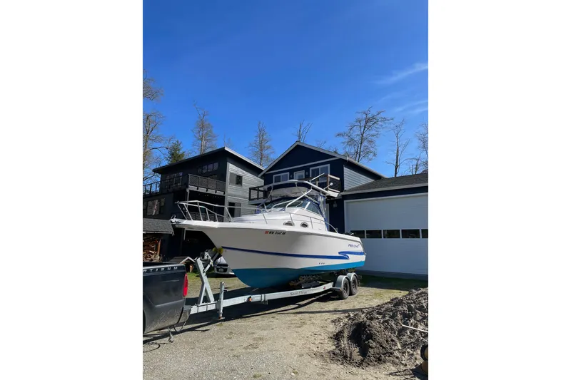 Slide: The Image of 2002 Pro-Line 260 Walkaround boat on trailer, parked near modern house under clear blue sky. - 5