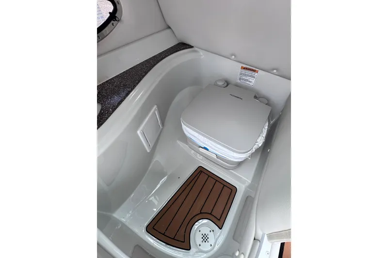 Slide: The Image of 2025 Crownline Eclipse E235 boat interior with portable toilet and wooden floor mat. - 29