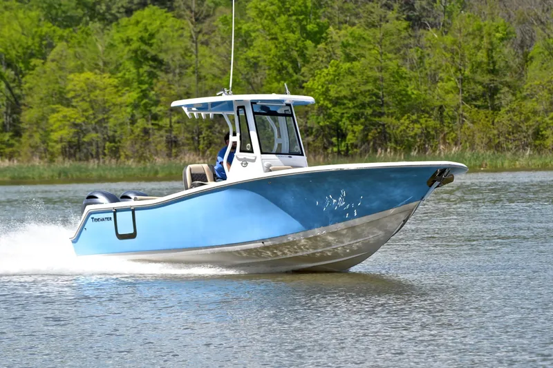 The Image of 2021 Tidewater 256 CC Adventure boat cruising on a serene lake with lush green background. - 1
