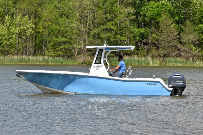Slide: The Image of 2021 Tidewater 256 CC Adventure boat cruising on a calm lake with lush green trees. - 10