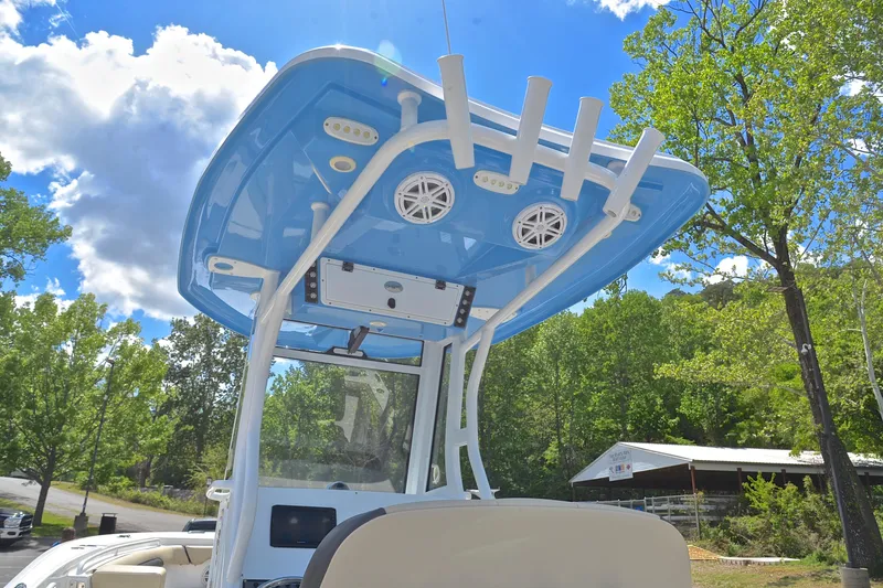 Slide: The Image of 2021 Tidewater 256 CC Adventure boat with blue T-top and rod holders, surrounded by trees. - 28