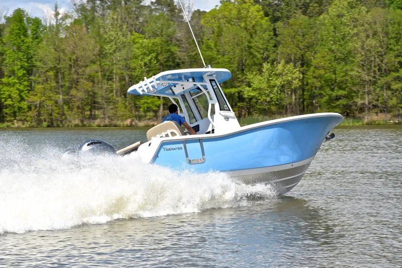 Slide: The Image of 2021 Tidewater 256 CC Adventure boat cruising on a lake with lush green trees. - 5