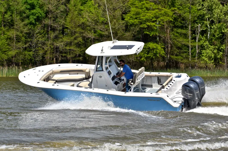 Slide: The Image of 2021 Tidewater 256 CC Adventure boat cruising on a lake with lush green trees. - 6