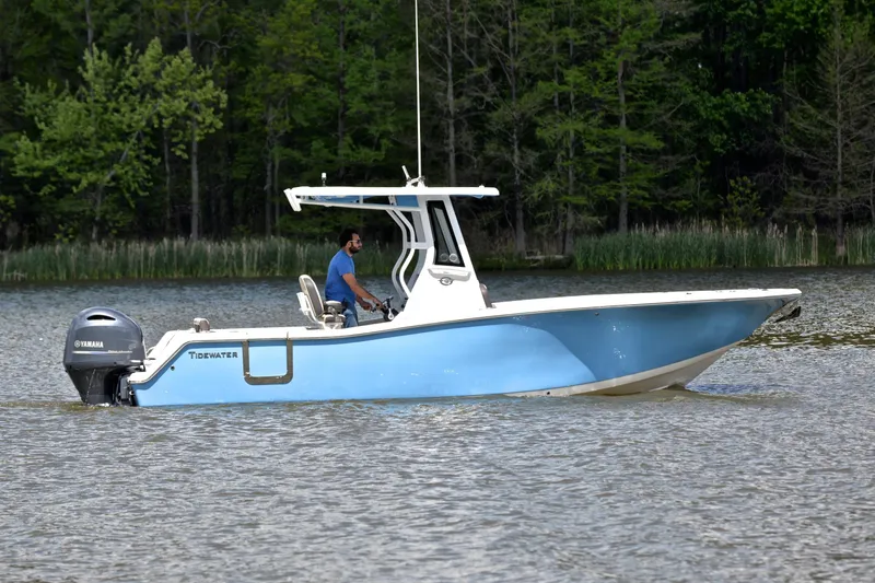 Slide: The Image of 2021 Tidewater 256 CC Adventure boat cruising on a lake with lush green trees. - 7