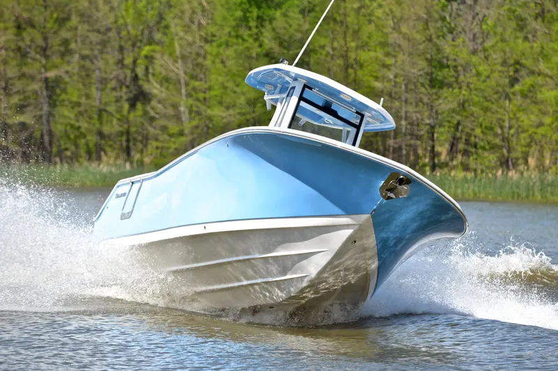 Slide: The Image of 2021 Tidewater 256 CC Adventure boat cruising on a lake with lush green trees. - 8