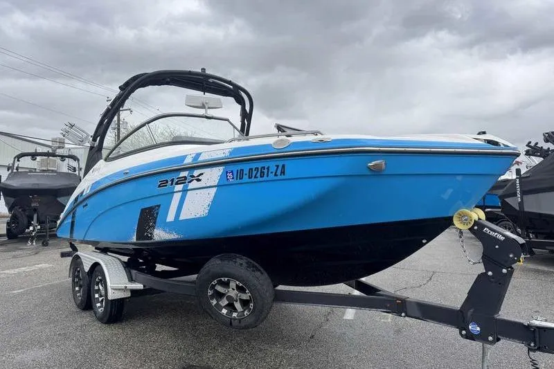 Slide: The Image of 2021 Yamaha Boats 212X in blue on trailer, parked outdoors under cloudy sky. - 15