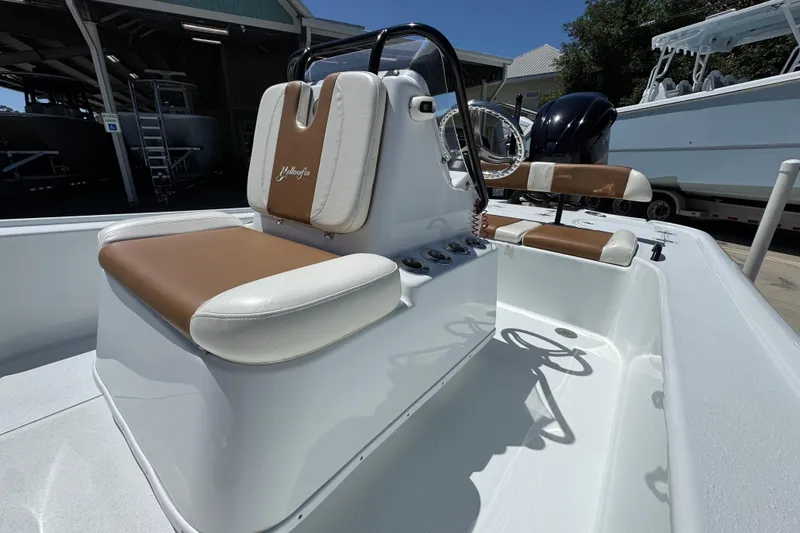 Slide: The Image of 2016 Yellowfin 21 Hybrid boat interior with brown and white seating, docked outdoors. - 26