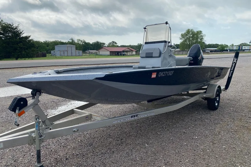 Slide: The Image of 2018 Xpress H20B Bay boat on trailer, parked outdoors under cloudy sky. - 2