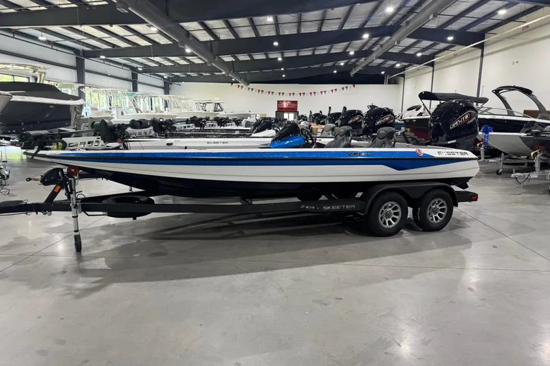 The Image of 2026 Skeeter ZXR21 SE boat in showroom, featuring sleek design and dual-axle trailer. - 0