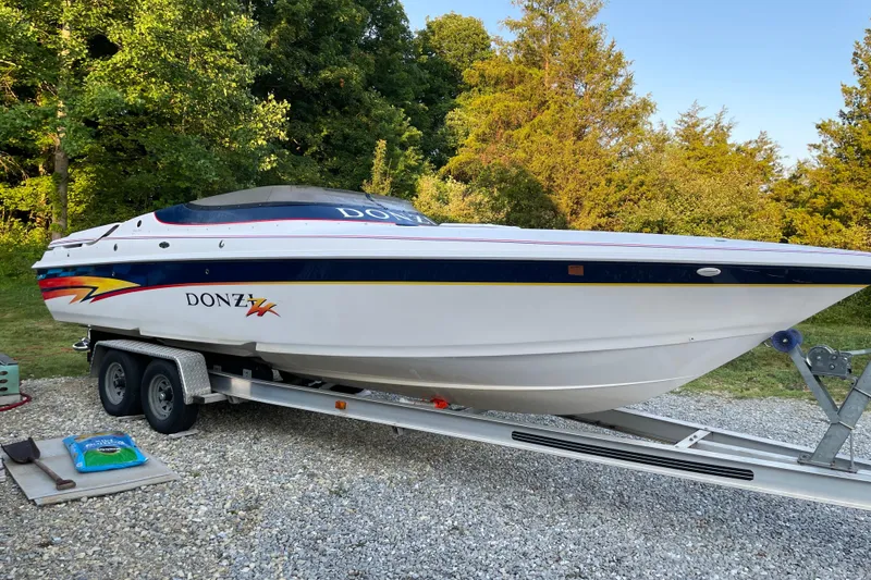The Image of 2001 Donzi 28 ZX speedboat on trailer, surrounded by trees and gravel. - 0