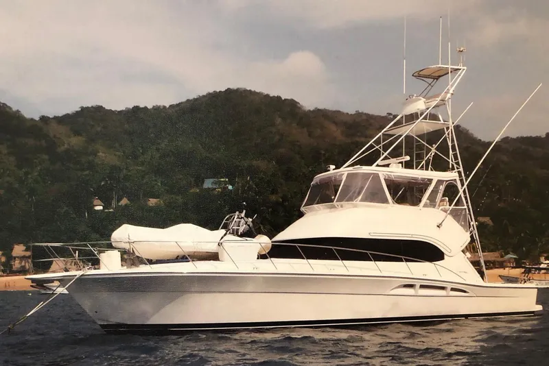 Slide: The Image of 2004 Riviera 51 Flybridge yacht anchored near lush, green hills. - 2