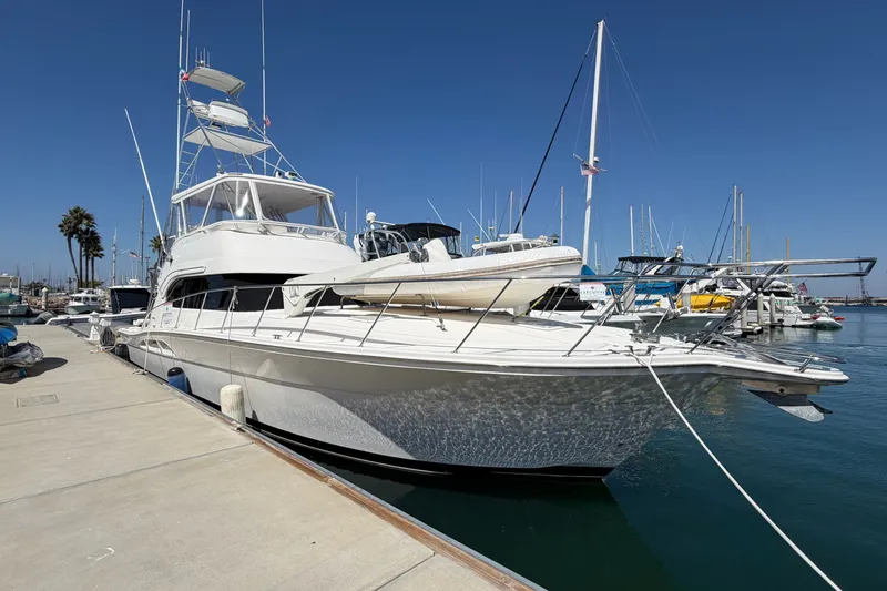 The Image of 2004 Riviera 51 Flybridge yacht docked at marina under clear blue sky. - 0