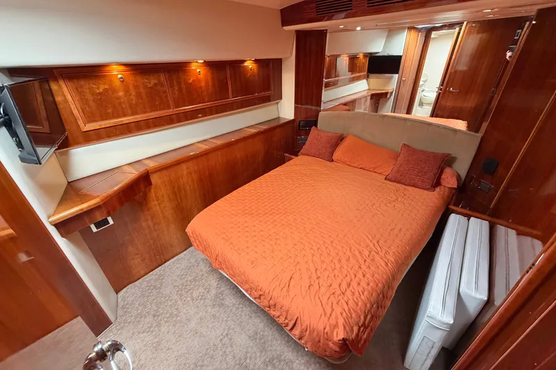 Slide: The Image of Luxurious 2004 Riviera 51 Flybridge cabin with orange bedding and elegant wood paneling. - 15