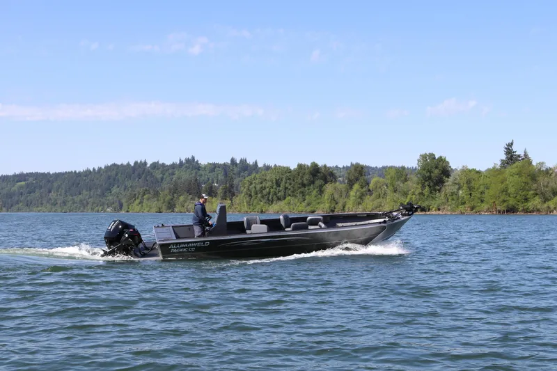 Slide: The Image of A 2027 Alumaweld Pacific CC 26 cruising on calm waters with a wooded shoreline in the background. - 2