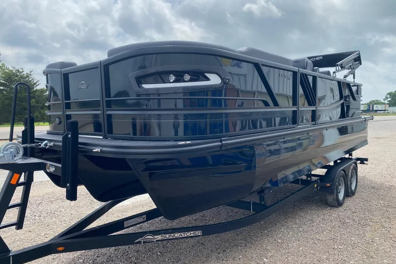Slide: The Image of 2026 SunCatcher Elite 324 SS pontoon boat on trailer, parked outdoors. - 2