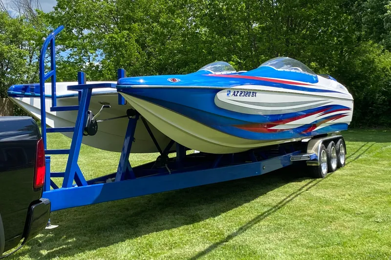 The Image of 2007 Eliminator 30 Daytona speedboat on trailer, vibrant blue and red design, parked on grass. - 1