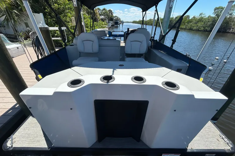 Slide: The Image of 2022 Godfrey Sweetwater 2286FS boat interior with seating and cup holders, docked by a river. - 23