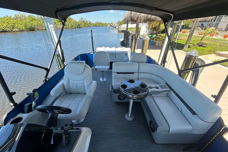Slide: The Image of 2022 Godfrey Sweetwater 2286FS pontoon boat interior with seating and table on a calm river. - 45