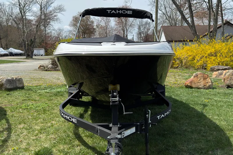Slide: The Image of 2025 Tahoe T18 boat on trailer, parked on grass with trees and rocks in background. - 2