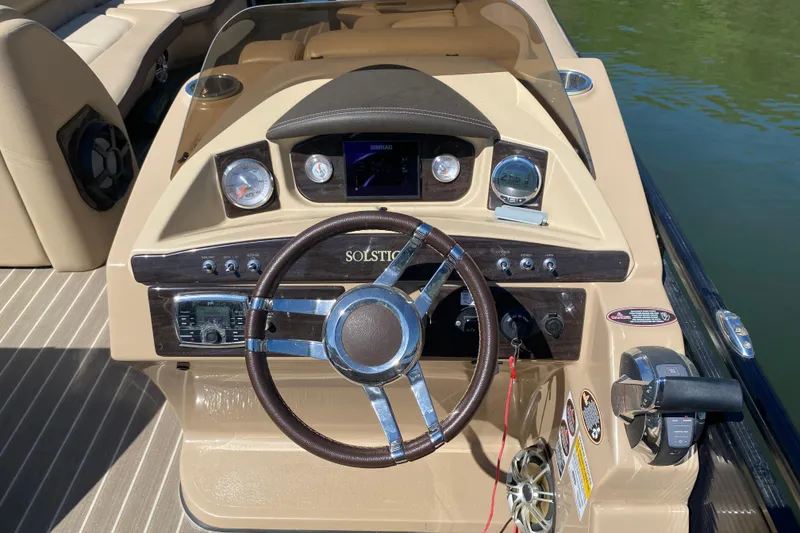 Slide: The Image of 2018 Harris Solstice 240 pontoon boat interior with beige seating, docked by a serene lake. - 21