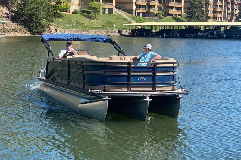 Slide: The Image of 2018 Harris Solstice 240 pontoon boat cruising on a lake near waterfront buildings. - 29