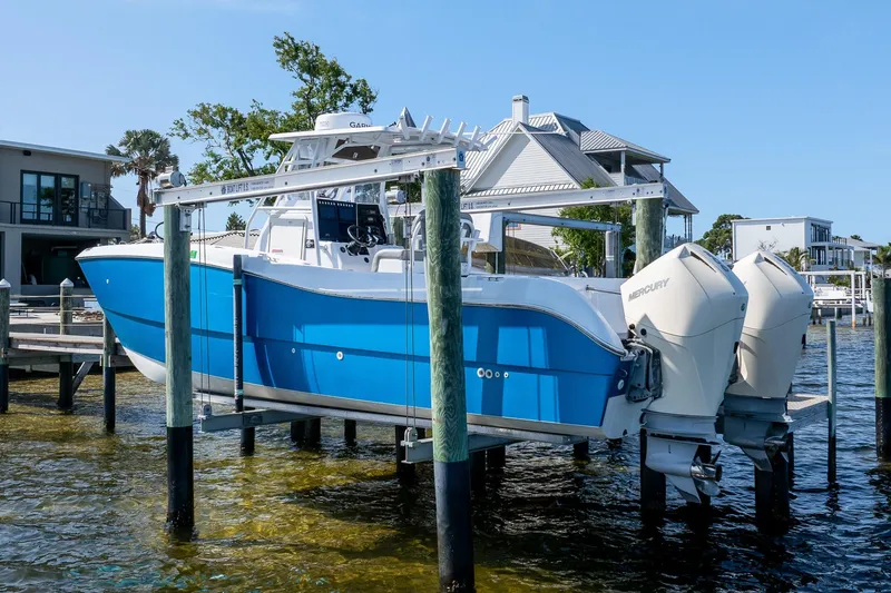 Slide: The Image of Blue 1998 World Cat 266 SF boat with twin Mercury engines on a lift by waterfront homes. - 2
