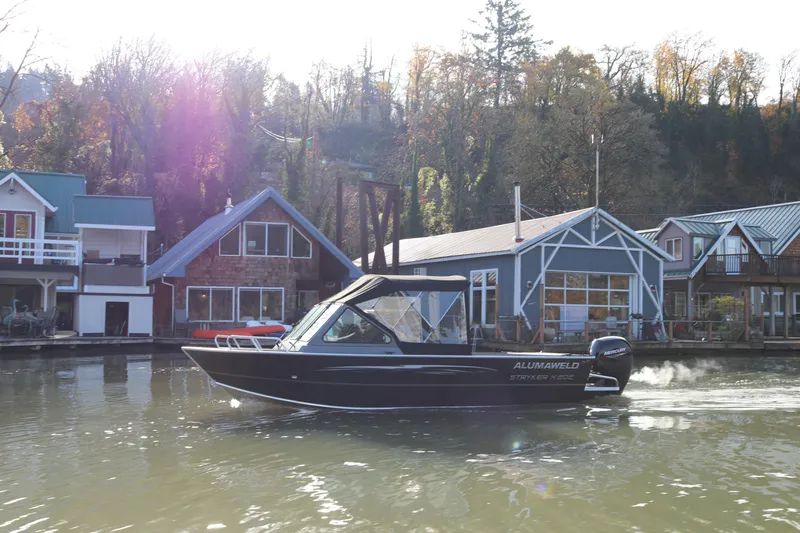 Slide: The Image of 2026 Alumaweld Stryker X202 boat cruising near waterfront homes in a scenic setting. - 4
