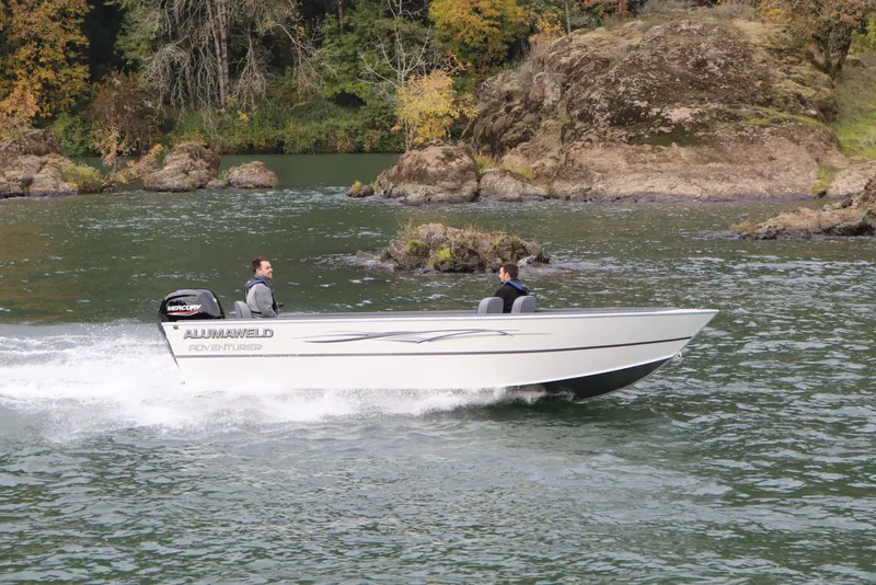 The Image of 2026 Alumaweld Adventurer 20 boat cruising on a scenic river with rocky shoreline. - 0
