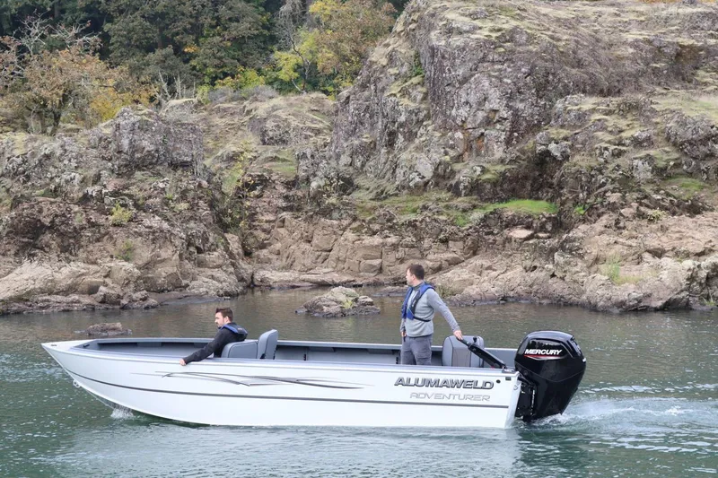 Slide: The Image of 2026 Alumaweld Adventurer 20 boat cruising near rocky shoreline. - 2