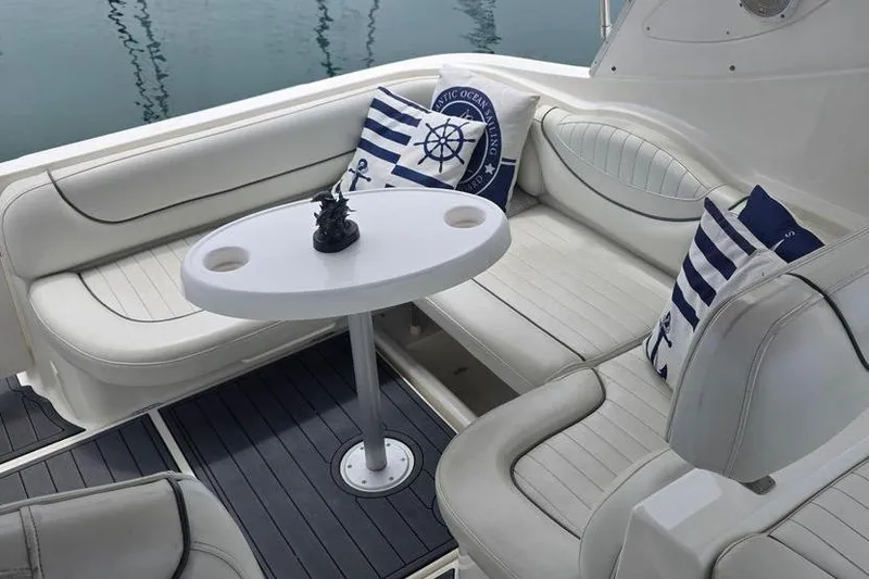 Slide: The Image of 2004 Maxum 3100 SE boat interior with white seating, nautical pillows, and a small table. - 8