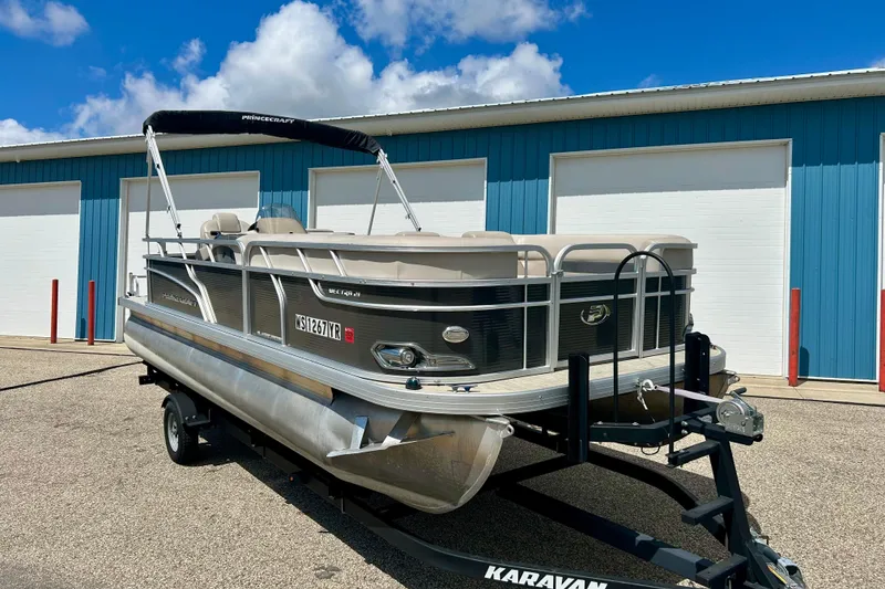 Slide: The Image of 2019 Princecraft Vectra 21 pontoon boat on trailer, parked near blue building. - 2